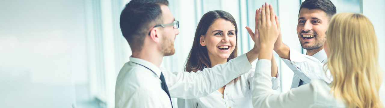 Cuatro personas chocando las manos en alto y sonriendo, en una oficina con ventanales